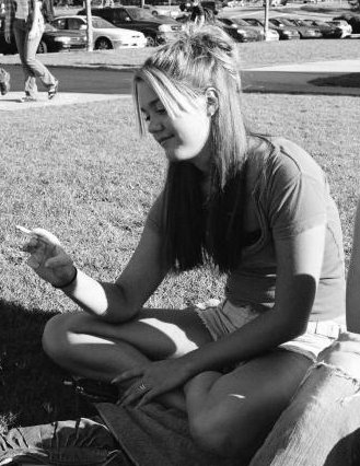 College girl sitting on the grass admiring her cigarette